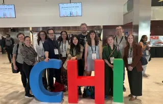 A photo of a group of Irish HCI researchers attending the CHI conference and standing by large colourful letters that read CHI