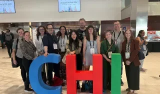 A photo of a group of Irish HCI researchers attending the CHI conference and standing by large colourful letters that read CHI